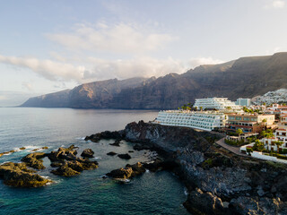 Cliffs of Los Gigantes behind a hotel on a rocky point. The basalt wall of Los Gigantes rises through morning cloud behind a white terraced hotel built onto a volcanic point.  © Oksana