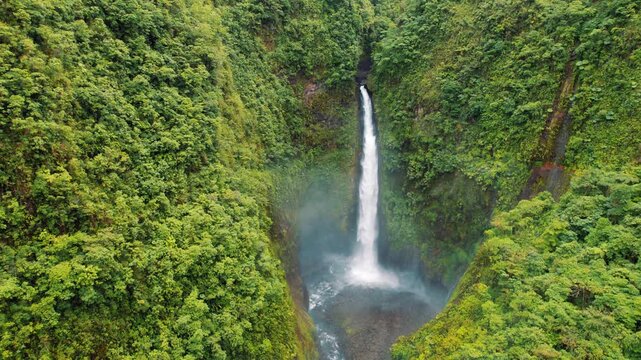 Powerful waterfall plunges into misty basin surrounded by steep green cliffs