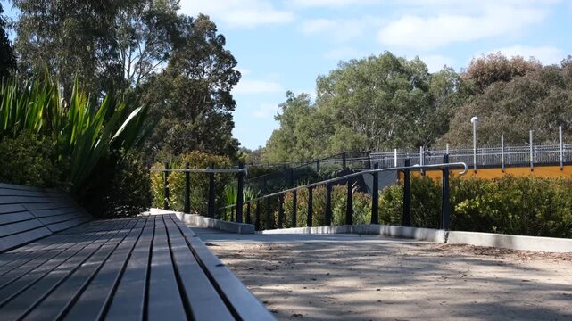 A wooden park bench seating leading to an accessible sloped pedestrian ramp with handrails in a public park reserve. Urban green spaces with seating and accessible infrastructure. Melbourne Australia