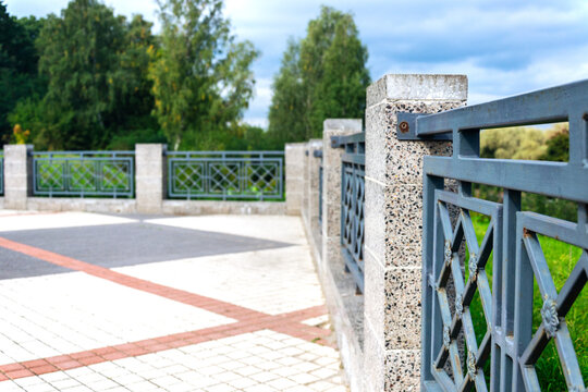 Selective focus on detailed forged steel fence pattern with blurry green park trees on background and copy space