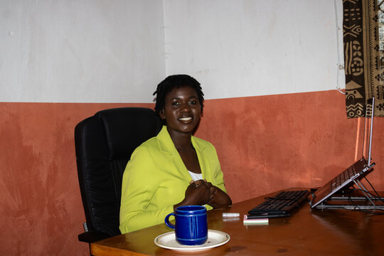Black woman in lime blazer at wooden desk, Blantyre office, Malawi &mdash; eye-level portrait of professional presence
