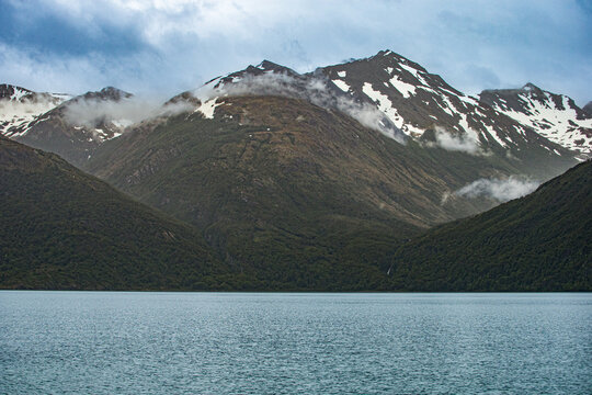 Scenic view of snowy mountains rising above a calm lake under a moody cloudy sky in patagonia