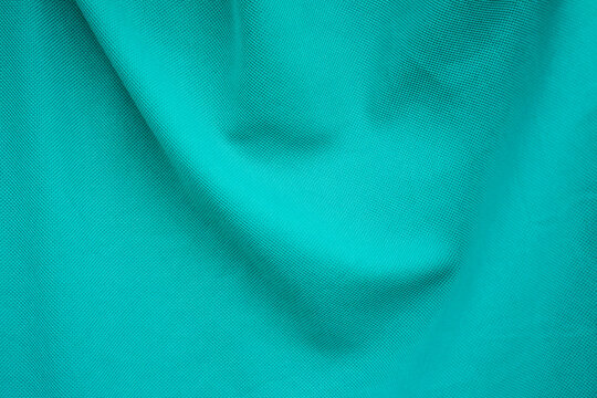 Close-up of turquoise green fabric texture with soft flowing waves, natural folds, and subtle woven details.