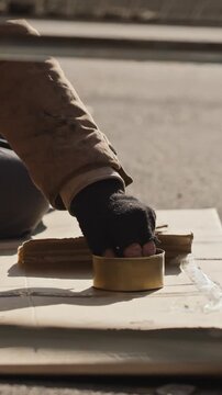 Vertical shot of homeless adult holding metal can while receiving coin donation on street. Visual fits charity campaigns, poverty awareness and social assistance projects