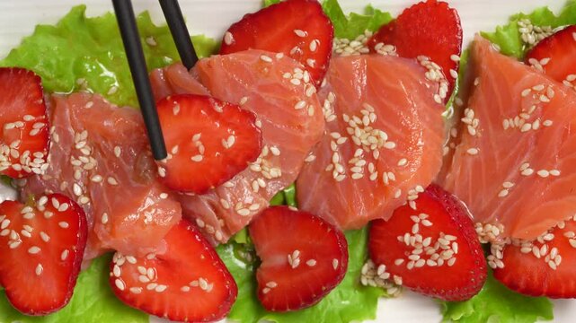 Salmon sashimi carpaccio with strawberries and sesame. Exotic salmon tataki salad with fresh strawberry slices and sesame seeds on a white plate with chopsticks. Minimalist gourmet seafood dish