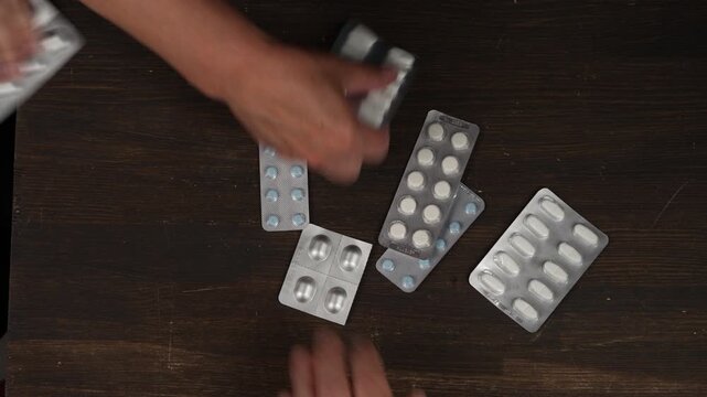 Many hands holding medicine blister packs. Diverse hands holding pharmaceutical blister packs and reach for medicine tablets on wooden background representing healthcare crisis or elderly care