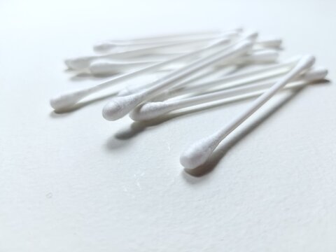 Close up of a pile of cotton swabs on a white background with blurred shadows.