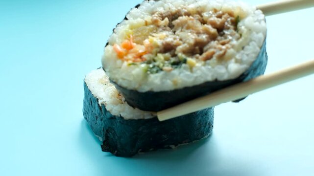 Korean gimbap roll and wooden chopsticks on blue background, close-up.