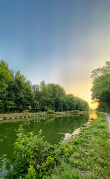 soft sunrise light along quiet canal pathway, gentle reflections, tree canopy opening to bright horizon, inviting scene