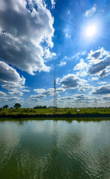 bright midday sky with towering clouds over still water, intense blues and crisp whites, open field facing distant electricity