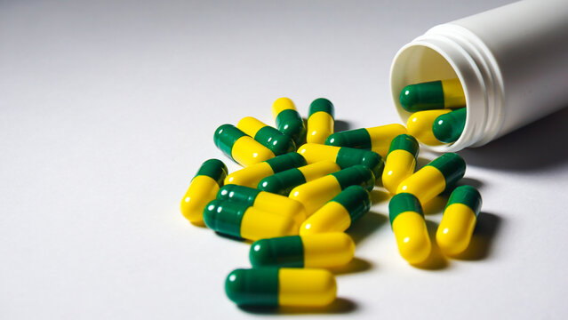Green yellow capsules spilled from white bottle. Medical concept. 