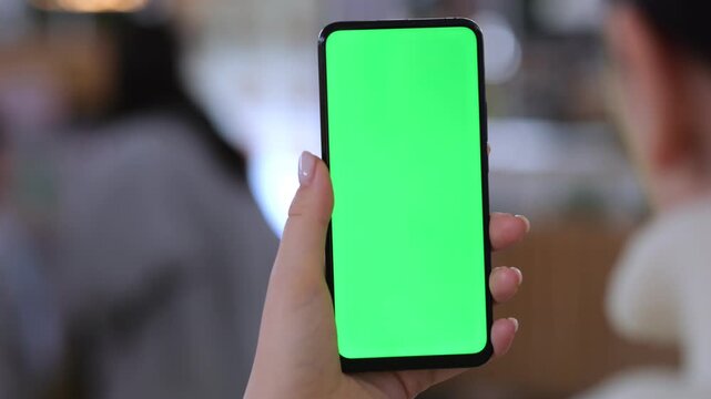 Hand holds smartphone with green screen. Blurred background shows indoor space. Three identical keyframes show same scene