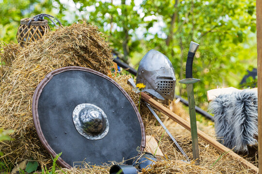 Authentic medieval knight equipment including a shield, sword, and helmet in a rural setting