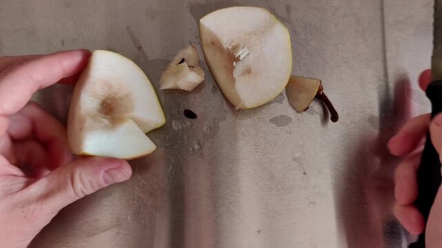 Woman's hand removing the stem from a ripe pear on a cutting board