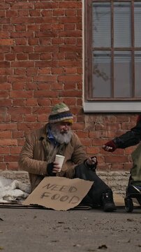 Vertical video of senior Caucasian homeless man sitting on sidewalk and receiving money donation. Clip suited for charity campaigns and social awareness projects