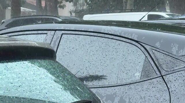 Extreme rainfall lashes parked vehicles during an intense urban storm, with water streaming across the windows and road surface, illustrating severe weather and difficult driving conditions