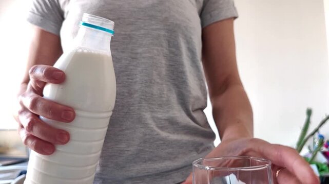 Woman transferring a milk bottle between hands and picking up an empty glass