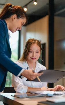 Asian supervisor and mentor guiding intern through career development process inside professional office space