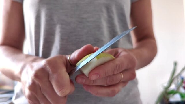 Woman peeling a ripe pear with a kitchen knife on a cutting board