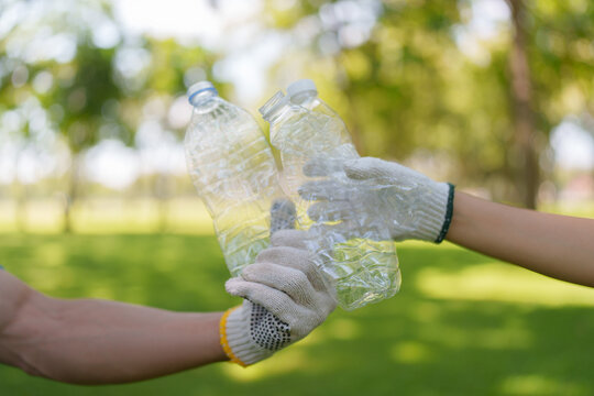Cropped gloved hands of volunteers clinking plastic bottles for recycling and teamwork concept