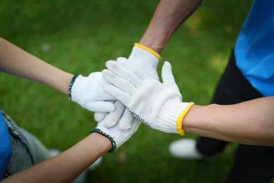 Volunteer team stacking hands in protective gloves for community cleanup and teamwork