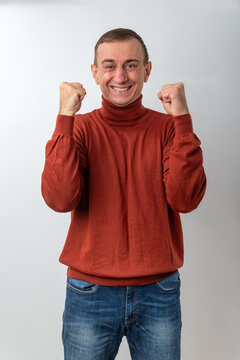 Happy man raising clenched fists, celebrating victory and achievement while expressing excitement and positive emotions standing against a white background