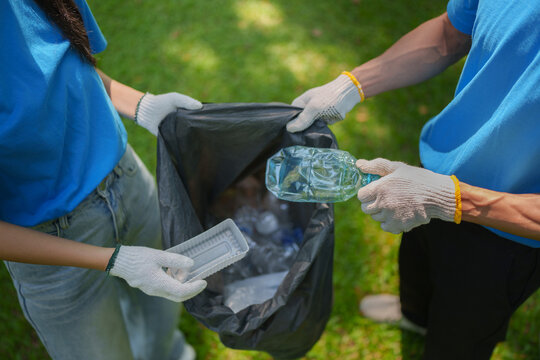 Volunteers collecting plastic waste in garbage bag for park cleanup drive
