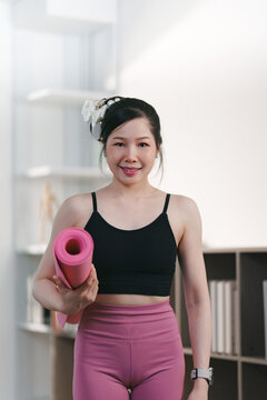 Portrait of smiling Asian woman holding yoga mat for fitness lifestyle
