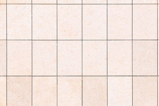 Beige rectangular stone tiles forming a seamless grid pattern, creating a neutral and clean architectural surface with subtle texture and dark grout lines