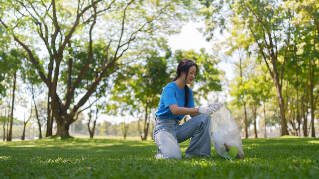 Asian female volunteer picking up trash and plastic waste in green park