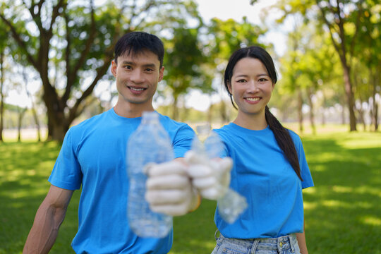Happy Asian volunteers holding plastic bottles during park cleanup for environmental recycling