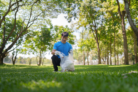 Asian male volunteer collecting plastic waste into trash bag for park cleanup