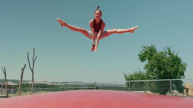 A girl is doing the splits on a trampoline outdoors