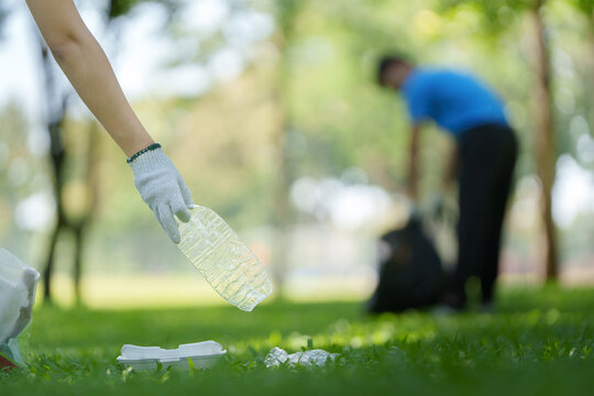 Volunteer hand picking up plastic bottle litter for park environment cleanup