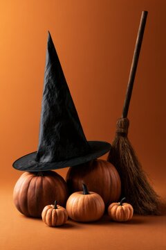 Halloween witch hat, broom, and pumpkins on orange background, vertical