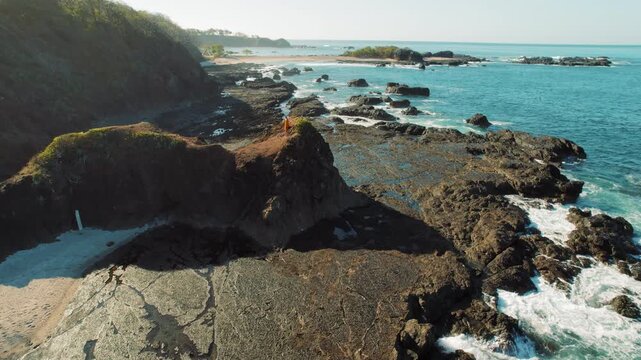 Aerial view of woman walking on rocky outcrop by ocean waves in Costa Rica