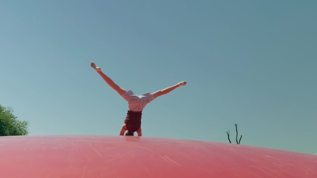 A girl does a handstand on a trampoline outdoors summer slow motion