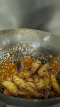 Golden fried potato wedges tumble from a skimmer into a wok containing a glossy red sauce.