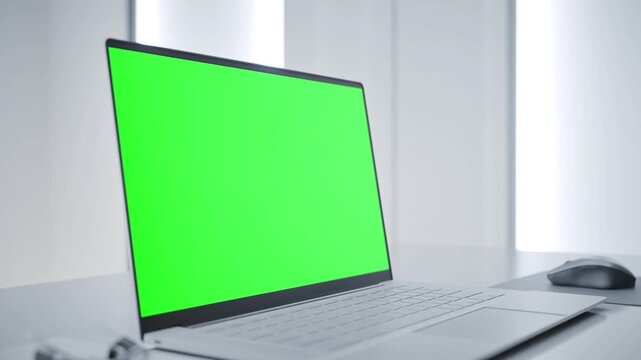 Laptop with Green Screen on White Desk in Modern Clean Tech Lab Interior