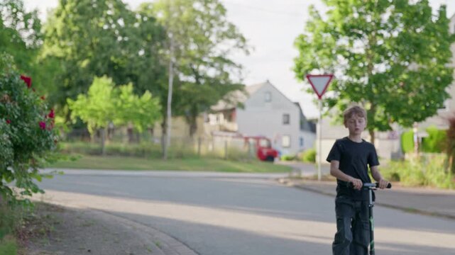 Unrecognizable boy riding kick scooter in village along a quiet residential street in a rural village on a sunny summer day