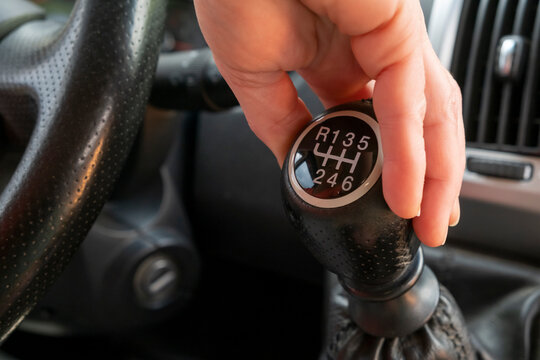Hand reaching for a manual gear shift in a car at a parking lot in the late afternoon
