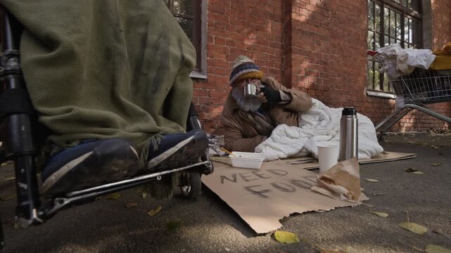 Caucasian senior homeless man drinking from cup while lying on street pavement. Perfect for non-profit charity campaigns, social welfare projects and poverty awareness videos