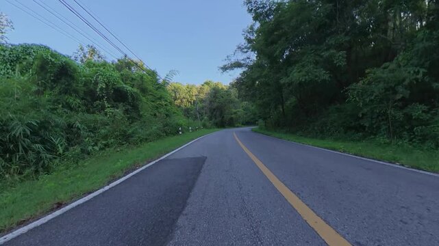 POV cycling footage on a winding mountain road surrounded by lush tropical forest, fresh asphalt, road markings and dense green vegetation.