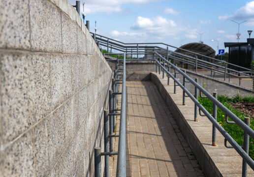 Outdoor concrete wheelchair ramp with metal handrails leading up to pedestrian zone on cloudy day