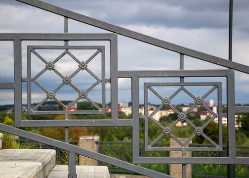 Ornate metal railing framing blurred city panorama under cloudy sky