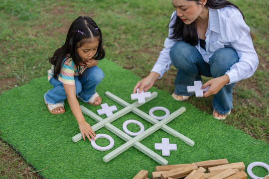 preschool child girl and mother playing tic tac toe game on green mat
