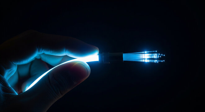 Close up of a hand holding a glowing blue fiber optic cable for high speed data transmission on black background