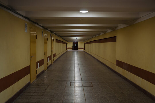 Long symmetrical tunnel of empty public pedestrian underpass with yellow walls and tile floor in city