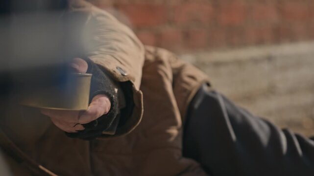 Senior homeless man receiving coin donation into tin can while sitting outdoors. Visual asset fitting charity campaigns, social welfare documentaries, and poverty awareness videos
