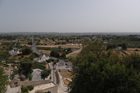 A view of the countryside in the Itria Valley, Puglia. The rural landscape features typical stone structures with conical roofs known as *trulli*, surrounded by dry-stone walls, ancient olive trees, a